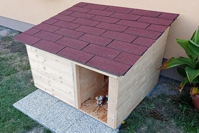 Dřevěná psí bouda s červenou střechou na trávníku.