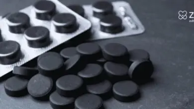 Černé tablety aktivního uhlí rozsypané na tmavém povrchu.