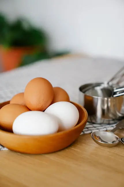 Hnědá i bílá vejce v dřevěné mísce s kuchyňskými nádobami.