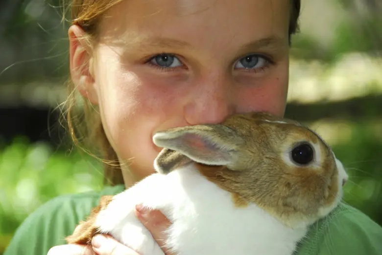 Dívka drží králíka v náručí na pozadí zelené přírody.