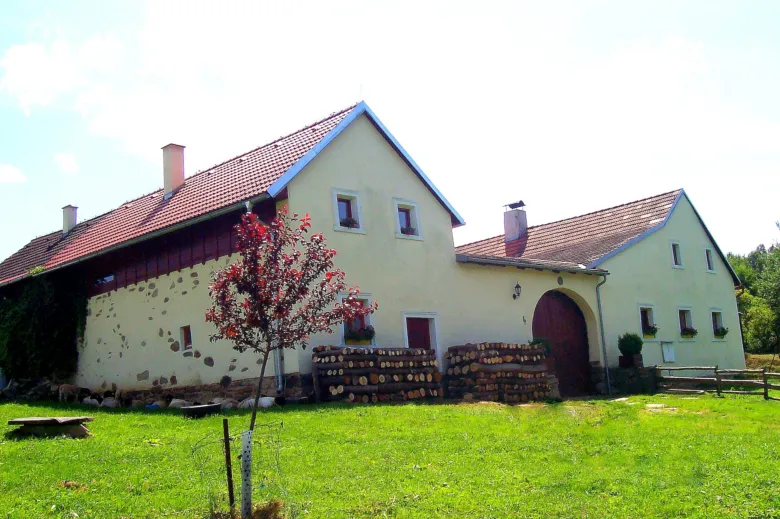 Farma s ovčínem před žlutou stodolou na zelené trávě.