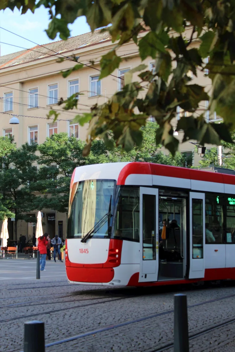 Červená tramvaj jede po kamenné ulici v městském prostředí.