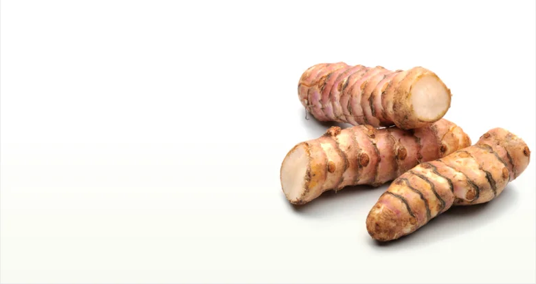 Tři kusy kořene topinamburu s jedním nakrájeným na ukázání vnitřní části.