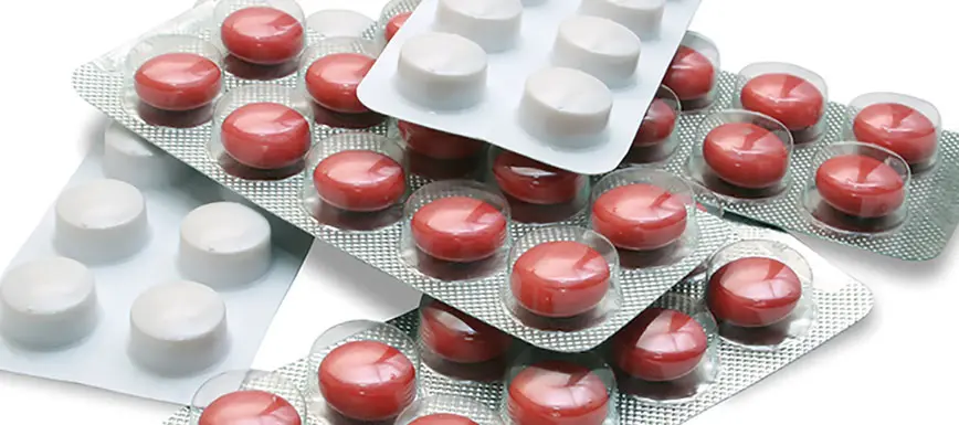 Červené a bílé tablety antibiotik v bublinkových obalech.