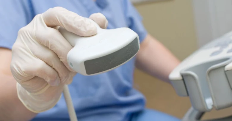 Rukou v rukavicích je drženo ultrazvukové sondu pro vyšetření prostaty.