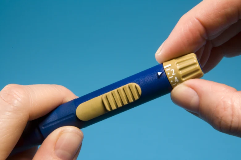 Ruka upravuje dávkování na modrém glukometru pro měření cukru.