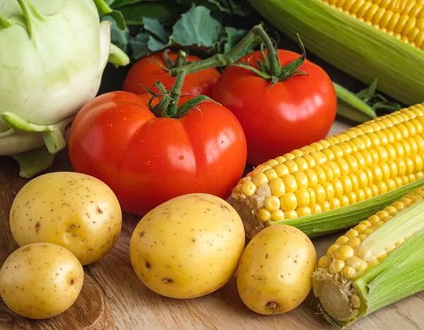 Čerstvá zelenina jako brambory, rajčata a kukuřice na dřevěném povrchu
